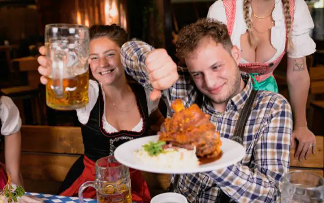 What is a Volksfest featuring a couple drinking a beer and eating a pork knuckle