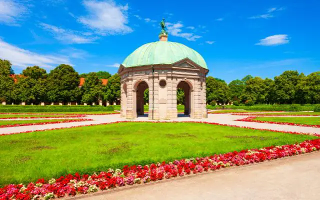 The Dianatempel Munich in the Hofgarten surrounded by colorful flowers with a blue sky background