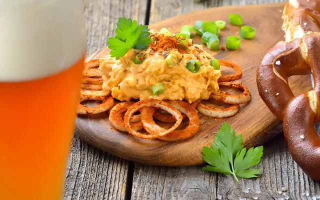 What Is Obatzda featuring a plate of this creamy orange Bavarian Cheese Delicacy with pretzel and beer